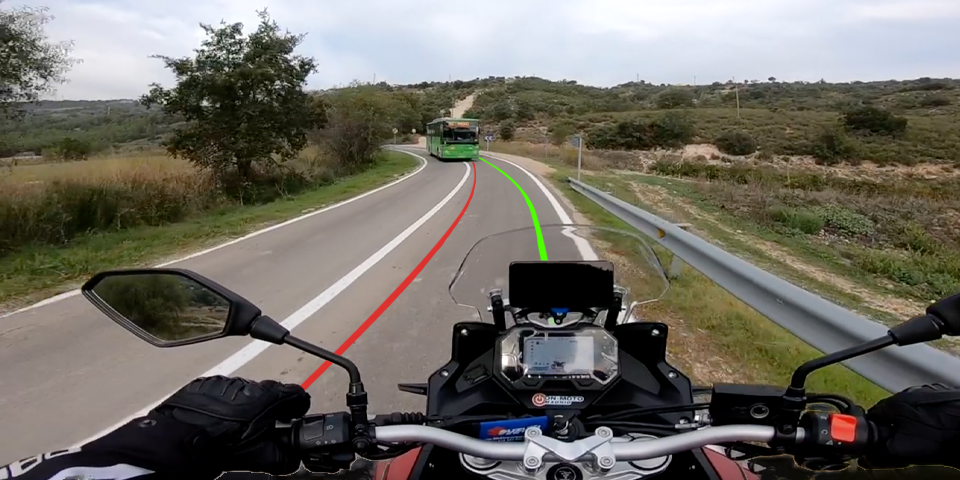 Vista onboard desde una motocicleta aproximándose a una curva a izquierdas con un autobús de frente. Se muestran dos opciones de trazada: una línea roja peligrosa por atacar pronto el vértice que lleva directo al accidente, y una línea verde que muestra la trazada defensiva correcta por el exterior para evitar el impacto y ganar opciones.