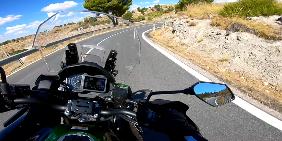 Motorista trazando una curva en carretera de montaña, aplicando el ángulo de ataque correcto y la mirada hacia el punto de fuga para maximizar la seguridad y evitar invadir el carril contrario.